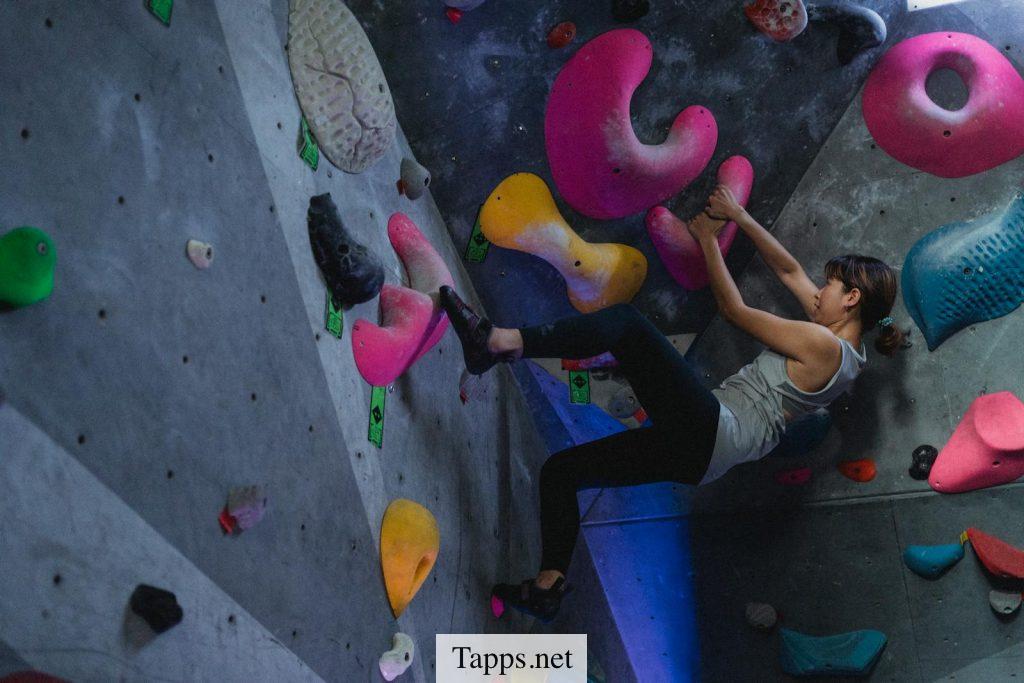 Side view full body of Asian female alpinist during workout on climbing wall in bouldering gym