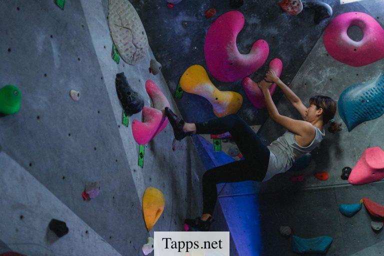 Side view full body of Asian female alpinist during workout on climbing wall in bouldering gym