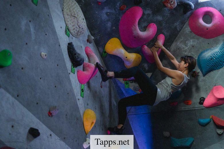 Side view full body of Asian female alpinist during workout on climbing wall in bouldering gym