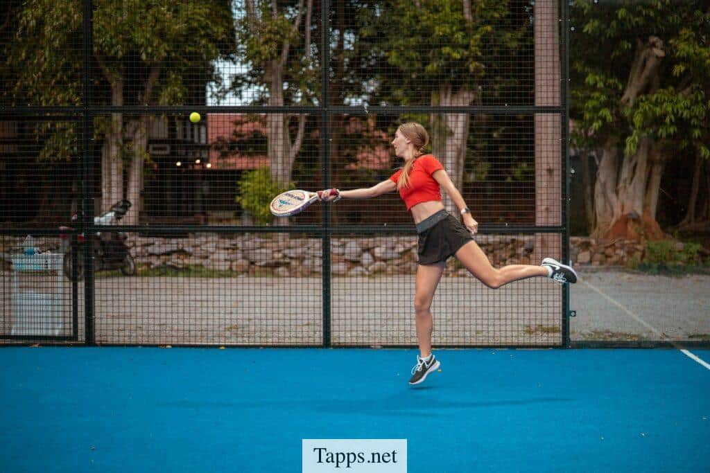 woman in red tank top and black shorts holding tennis racket